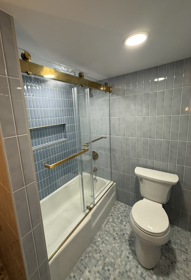 After renovation: tub with blue vertical tile and glass sliding door