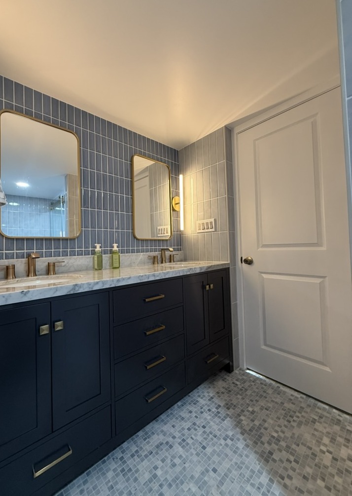 After renovation: navy double vanity with marble counter, gold hardware, and blue tile