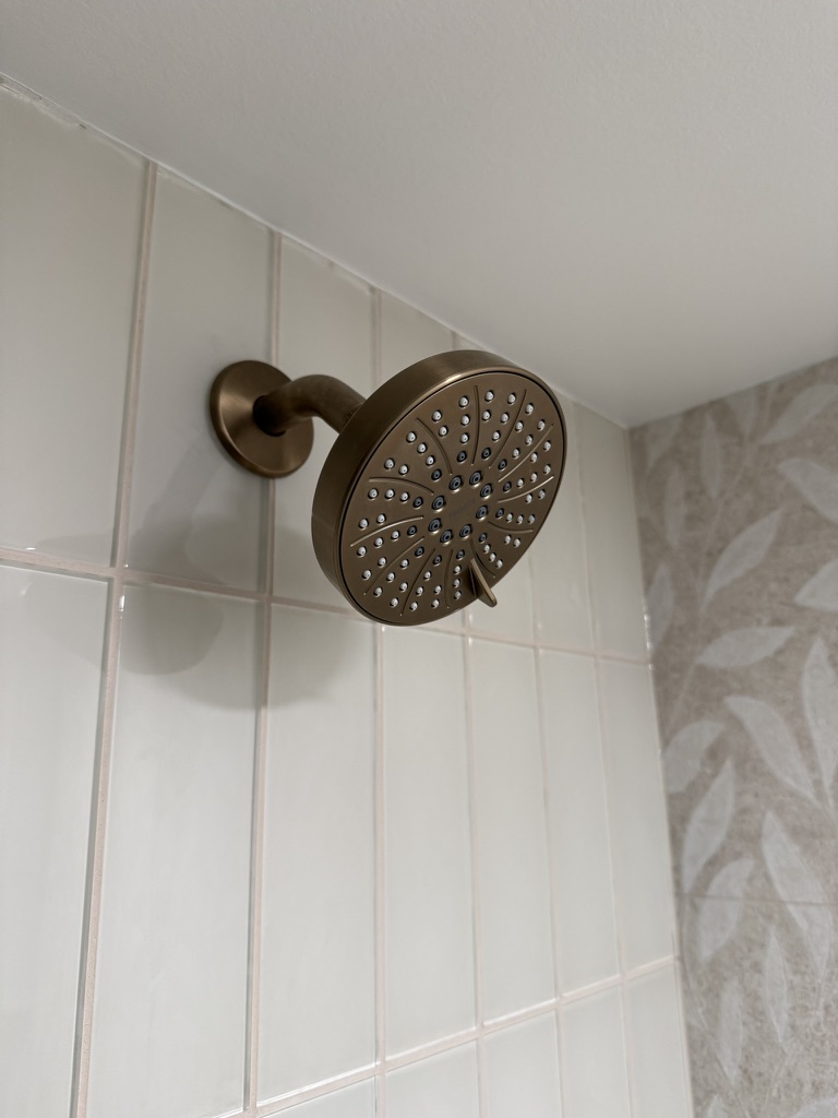 Brushed brass shower head on white subway tile