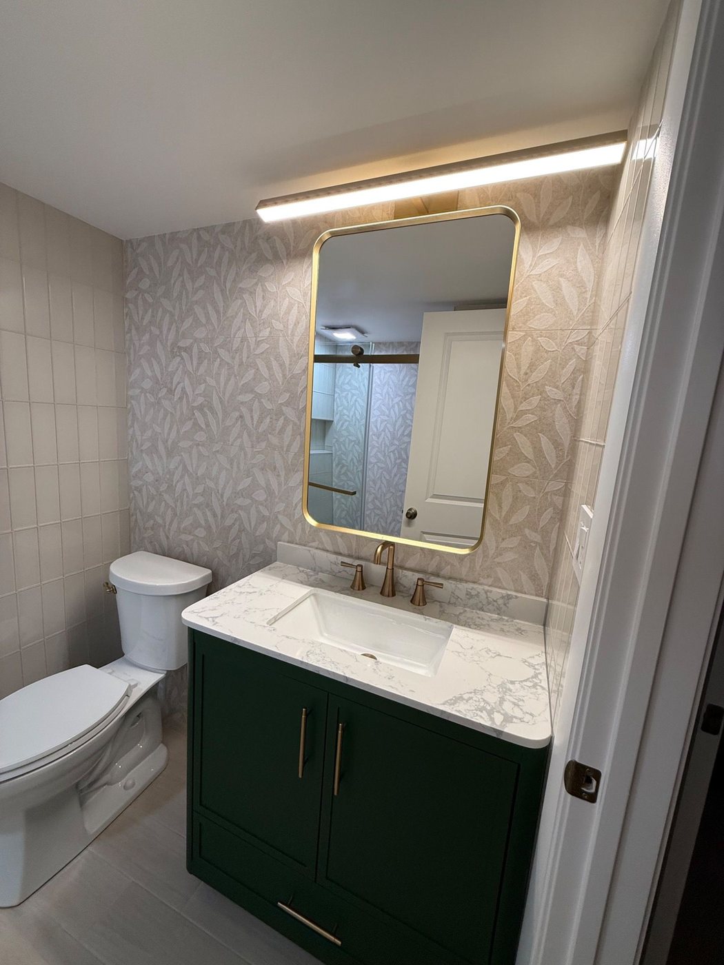 Green vanity with large backlit mirror and patterned wall tile