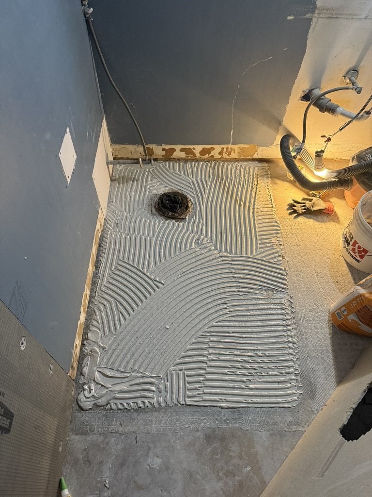 Shower floor mortar bed troweled ahead of tile with drain exposed