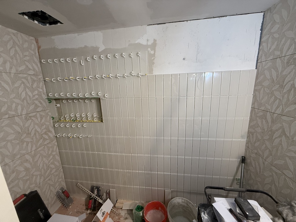 Subway tile install in progress with leveling clips and niche cutout