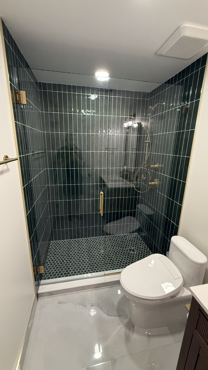 Finished bathroom with hunter green tile shower, black hex floor, and toilet seen across the room