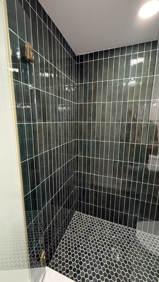 Corner view of the hunter green tile shower with black hex floor