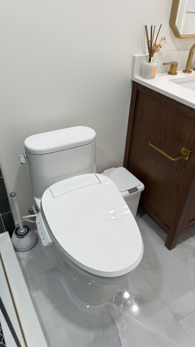 Finished toilet with vanity and shower glass in the background