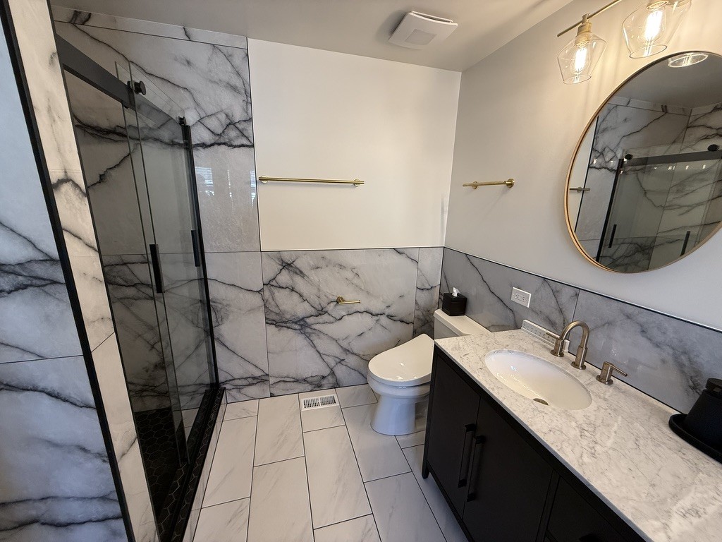 Wide bathroom view with the marble shower, toilet nook, and vanity corner