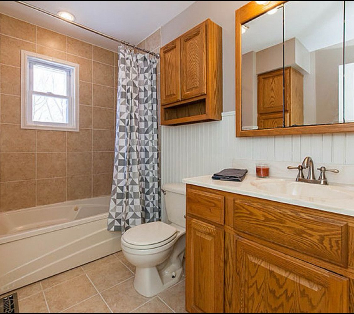 Before renovation: original tan tile bathroom with tub and oak vanity