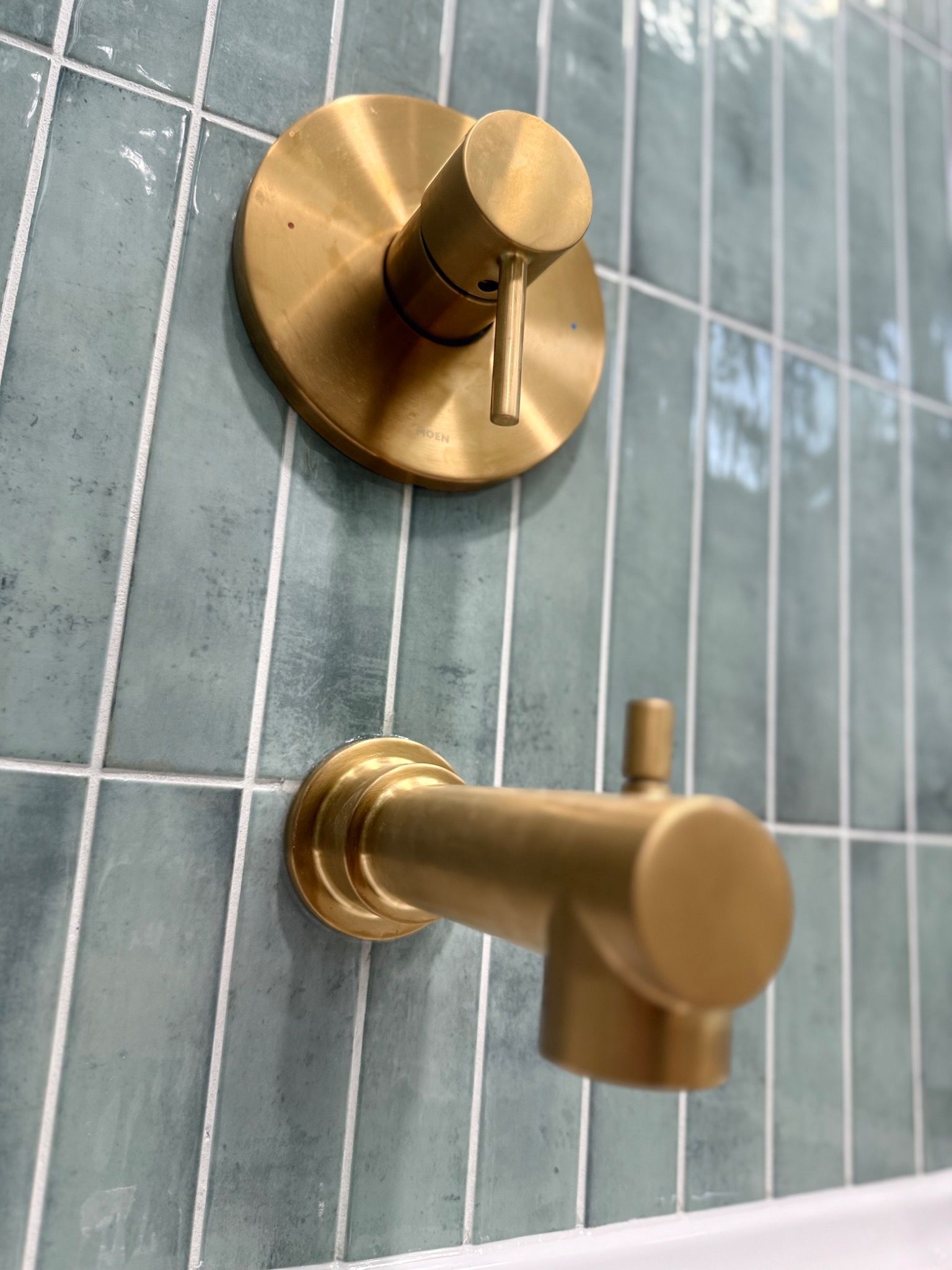 Brass shower handle and tub spout detail against green tile