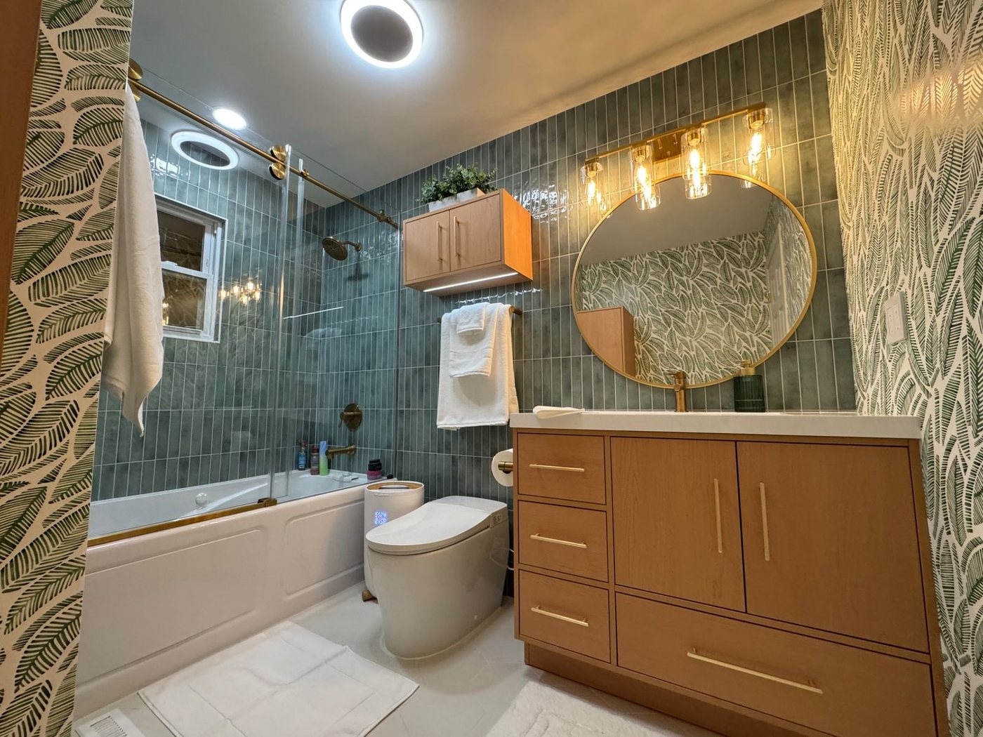 Finished tropical bathroom remodel with green tile, wallpaper, tub, and wood vanity from the main entry view