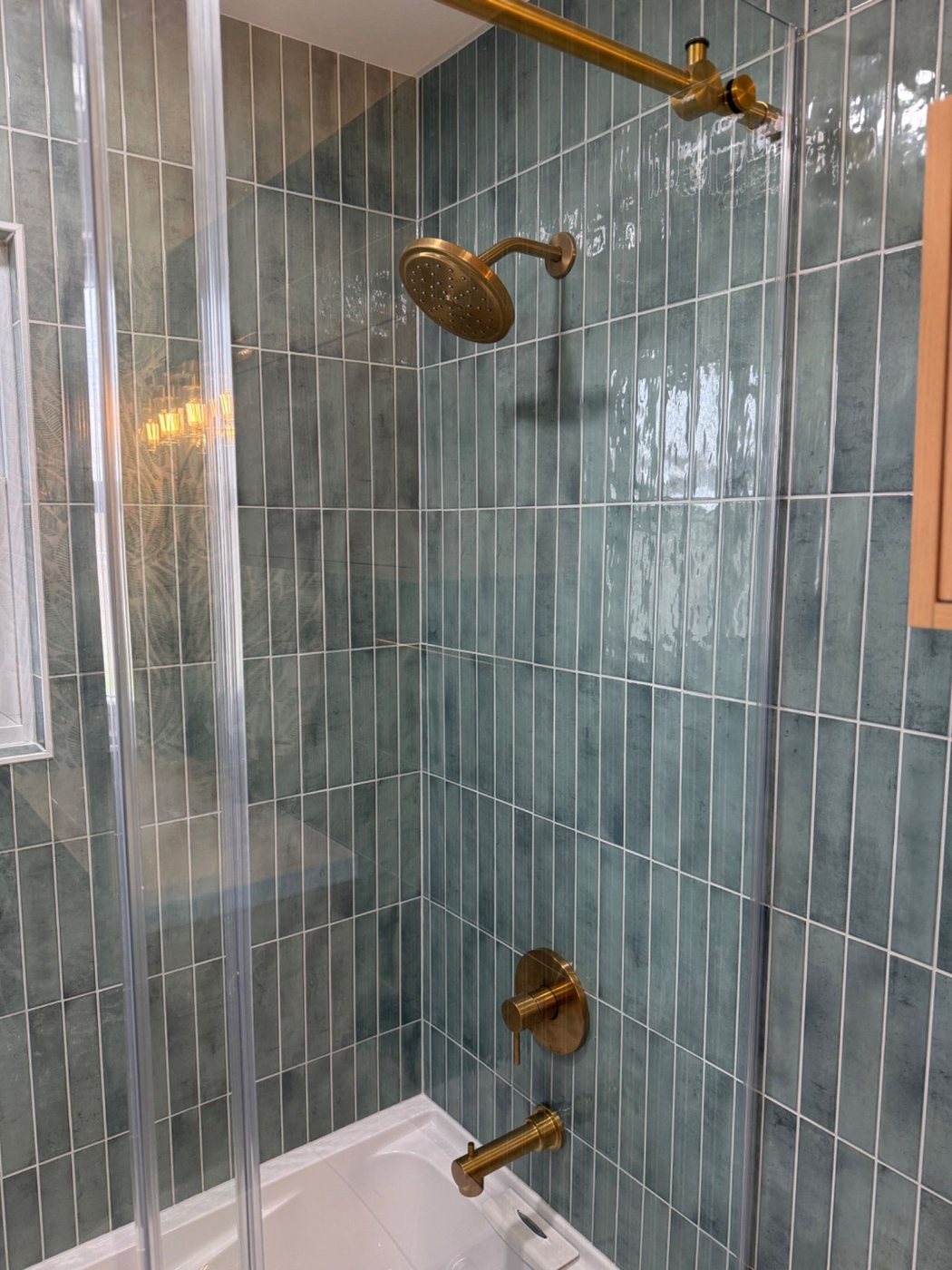 Closer view into tub and shower with green tile and brass fixtures