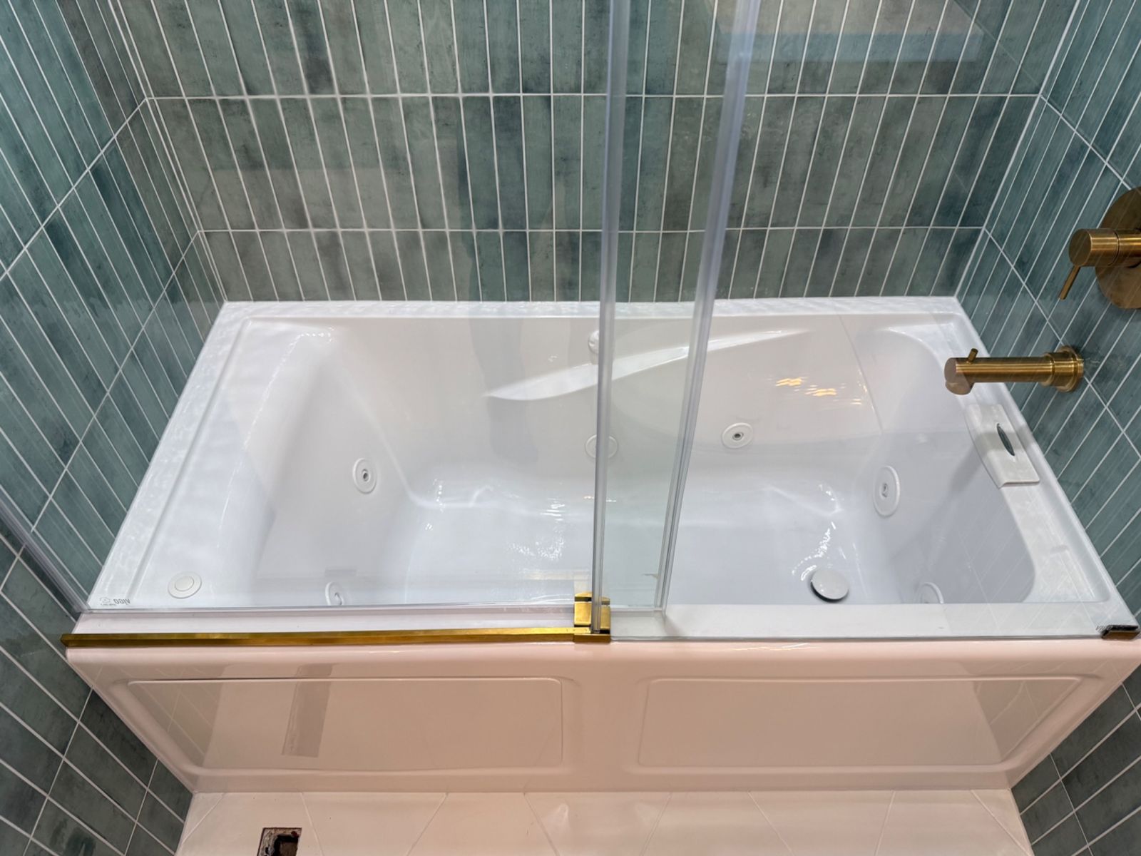 Jetted tub detail with glass panel and green tile wall