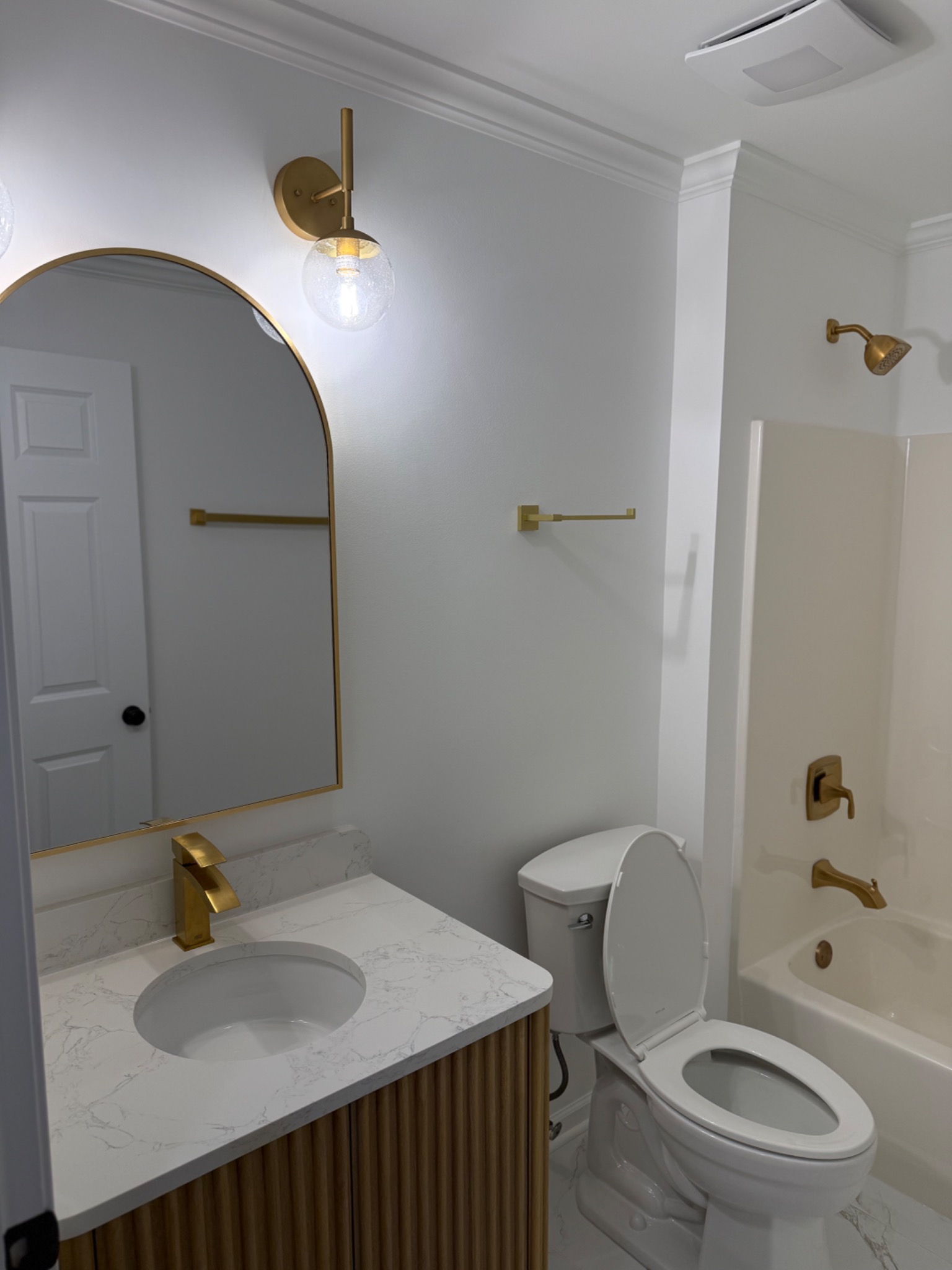 Vanity, mirror, and tub surround view in warm brass bathroom refresh