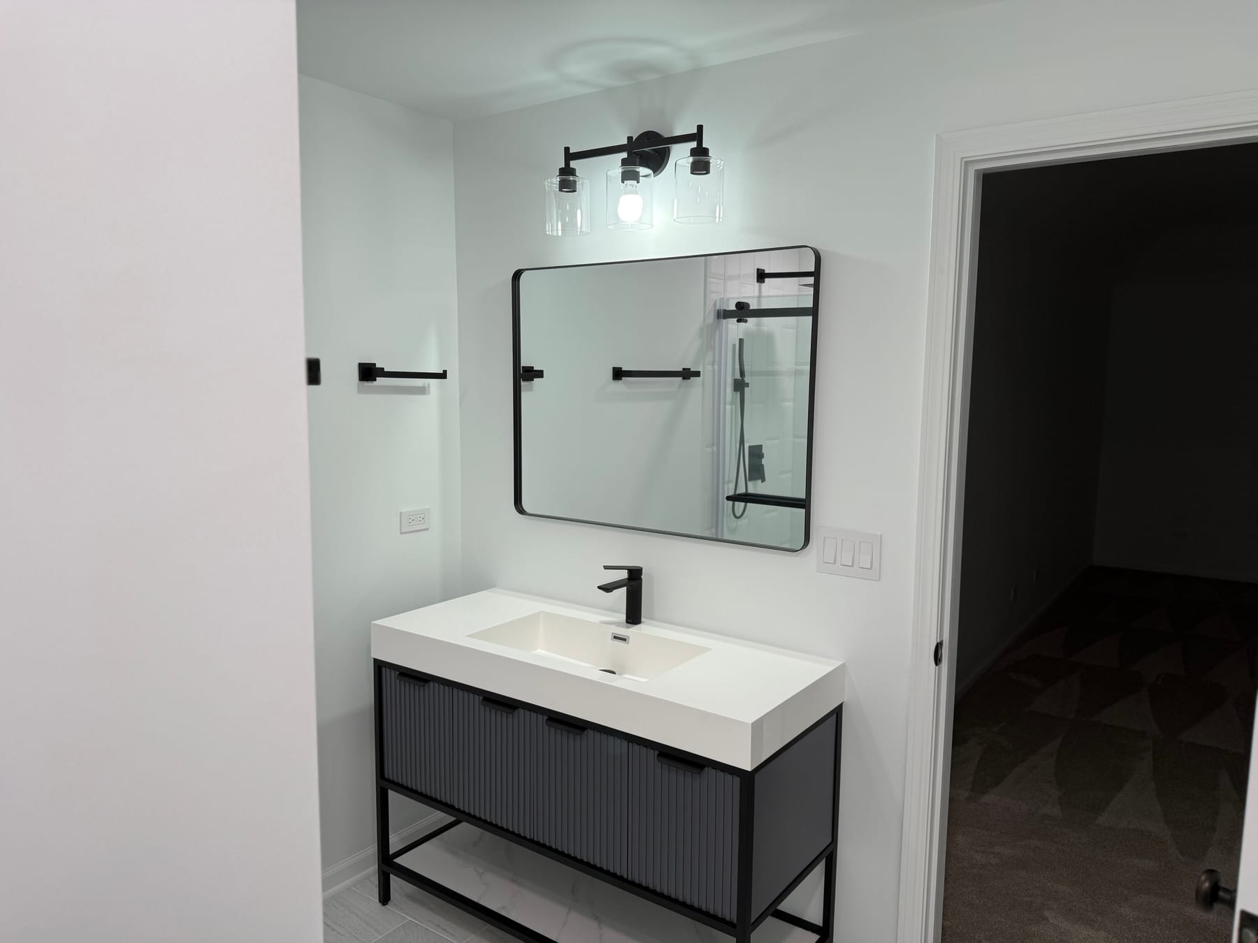 Modern black bathroom vanity with matching mirror, faucet, and three-light fixture