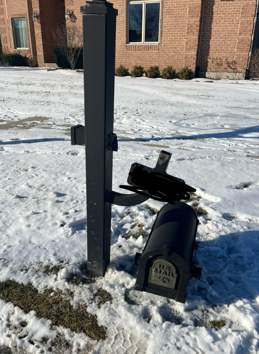Broken mailbox that needs repair on a snowy front lawn