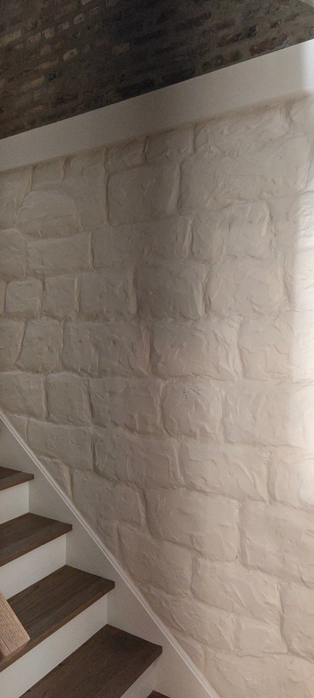 Finished decorative stone wall painted light color beside staircase