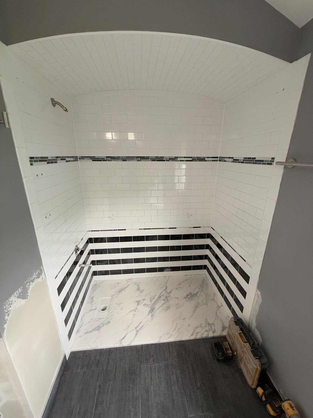 Open shower area during conversion with white subway tile and marble-look base