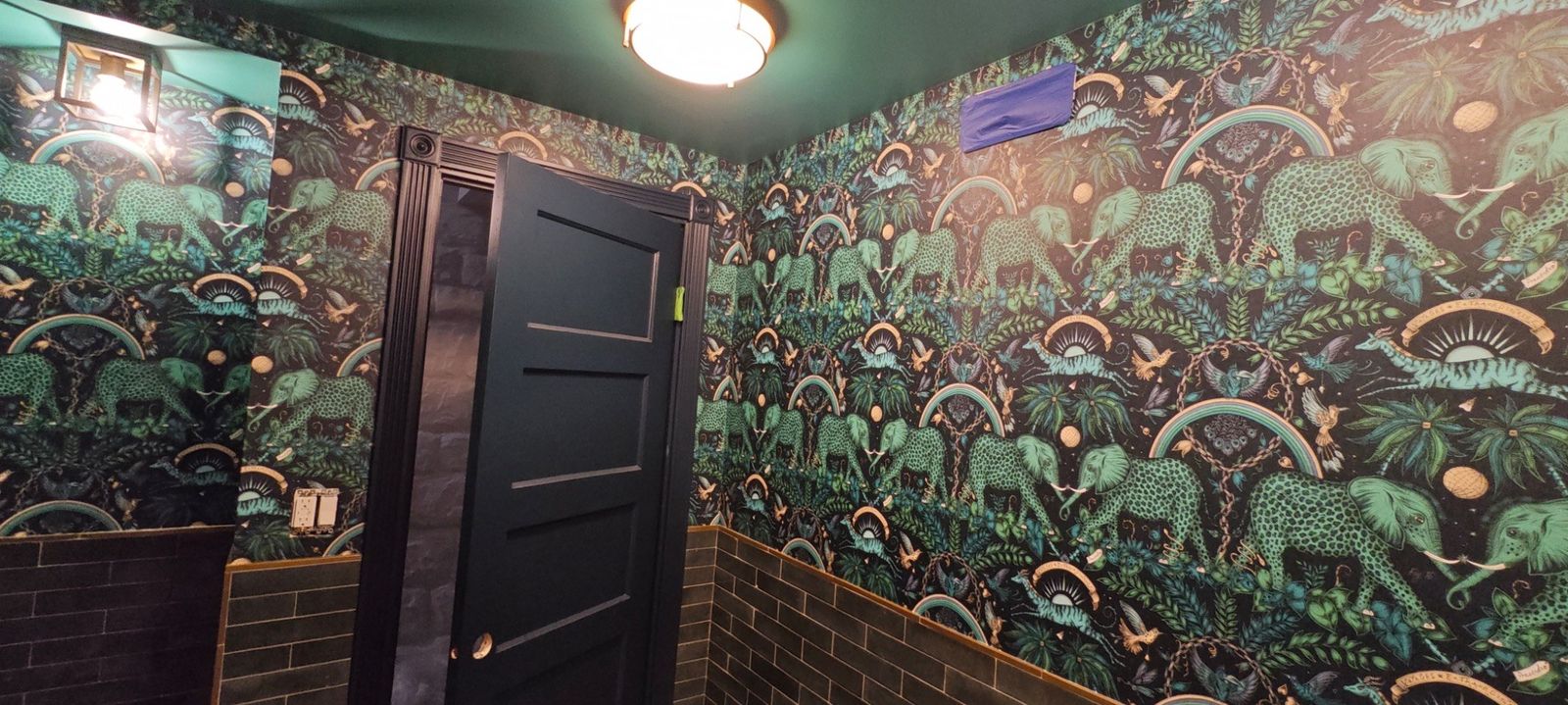 Dark tropical wallpaper installed in room with black door